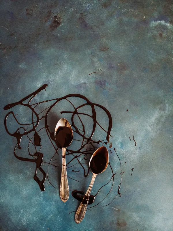 Two spoons with a dark sweet drizzle on a textured blue surface